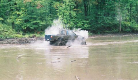 1977 Ford F-150 - This Ford F-150 is navigating a muddy, water-filled terrain with significant spray.