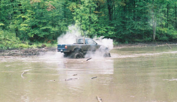 Dark blue Ford F-150 driving through mud and water, kicking up spray