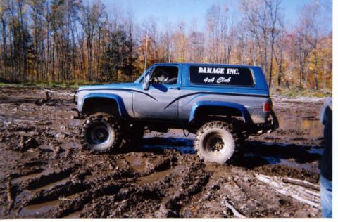 1977 Ford F-150 - This modified SUV is deeply stuck in a muddy off-road terrain, with trees in the background.
