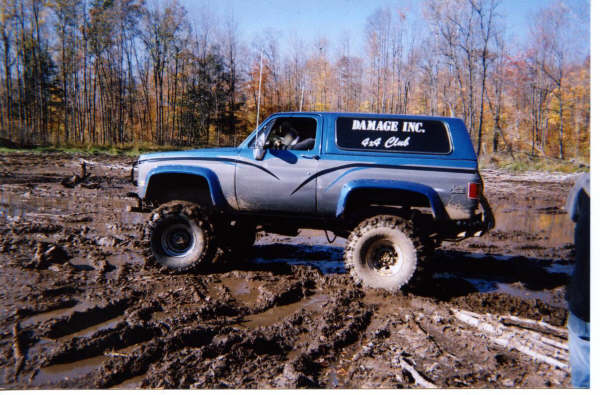 Blue and silver SUV with "DAMAGE INC. 4x4 Club" on window stuck in mud