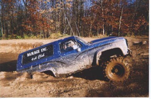 1977 Ford F-150 - A blue off-road vehicle is stuck in thick mud, with trees and dry foliage visible in the background.