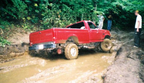 1977 Ford F-150 - A red Ford F-250 navigates a muddy trail with onlookers present.