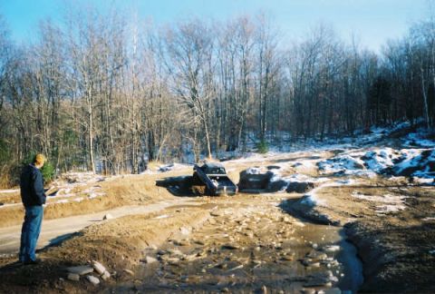 1977 Ford F-150 - A truck is stuck in a muddy, wooded area with patches of snow on the ground.