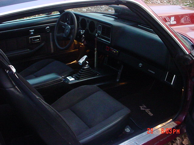 Black interior of a red coupe with bucket seats, floor shifter and round-gauge dashboard