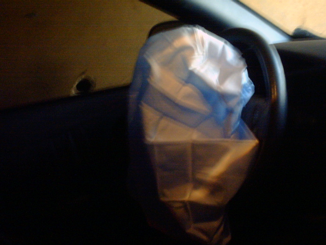 Deployed white driver airbag hanging from steering wheel inside a dark car interior