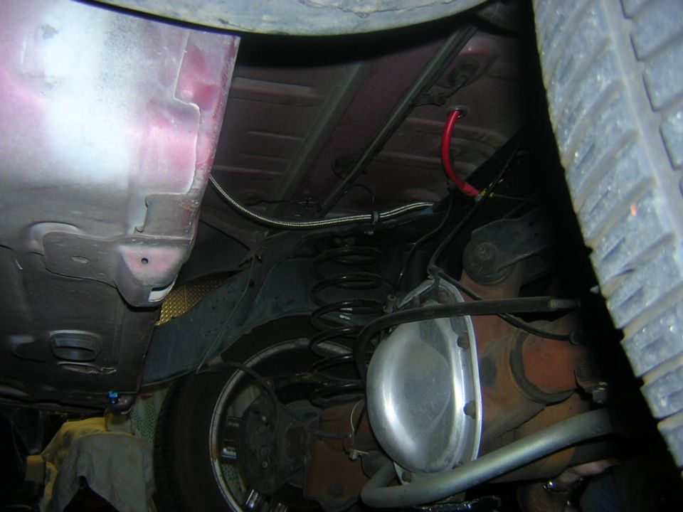 Undercarriage of a car showing suspension, differential, and tire. Red hose visible