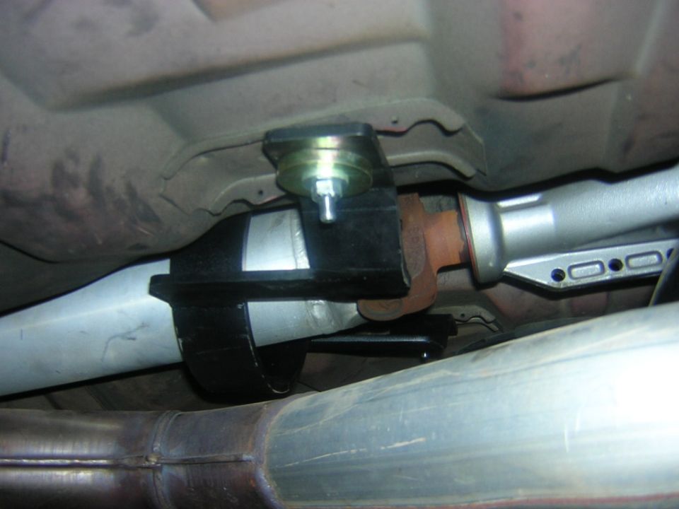 Driveshaft center support carrier bearing bracket underneath a car beside exhaust pipes