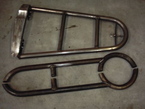 1978 Ford Bronco - Two bare welded steel tube fabrications lying on a concrete shop floor: a triangular skid-plate/bumper frame with a flat mounting plate and…