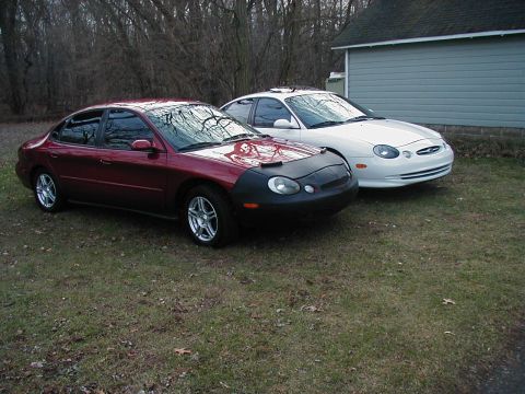 1997 Ford Taurus - Two Ford Taurus sedans are parked side-by-side on a grassy area next to a building.