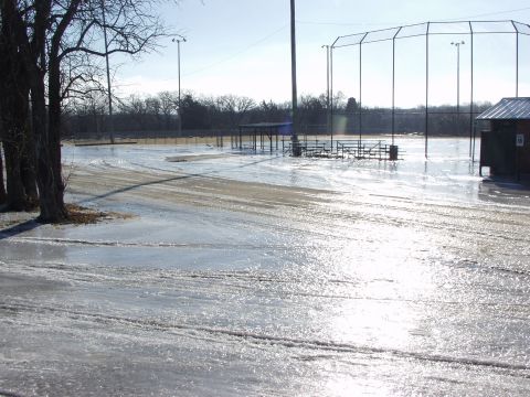 1979 Ford Bronco - A baseball field is covered in ice, with tire tracks visible on the frozen surface.