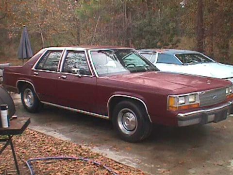 1994 Ford Crown Victoria - Maroon sedan parked outdoors next to a white car. The sedan's body style suggests an early 1990s model.