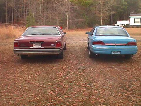 1994 Ford Crown Victoria - Two sedans, a blue 1994 Ford Crown Victoria and a red one, are parked side-by-side on a gravel lot.