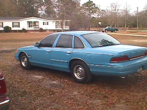 1994 Ford Crown Victoria - A blue 1994 Ford Crown Victoria is parked on a gravel lot in front of a mobile home.