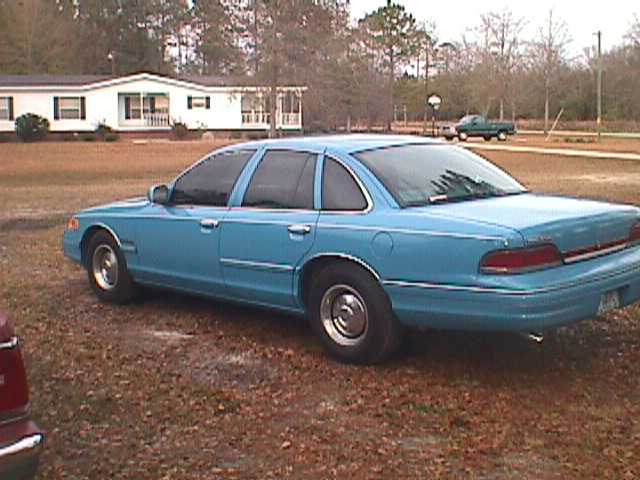 Blue 1994 Ford Crown Victoria parked in a yard with a house and trees in the background