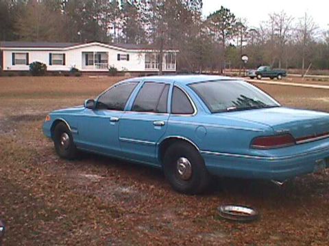 1994 Ford Crown Victoria - A blue sedan is parked outside a mobile home on a cloudy day.