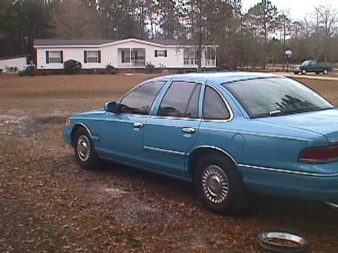 1994 Ford Crown Victoria - A blue sedan is parked in front of a house on a cloudy day.