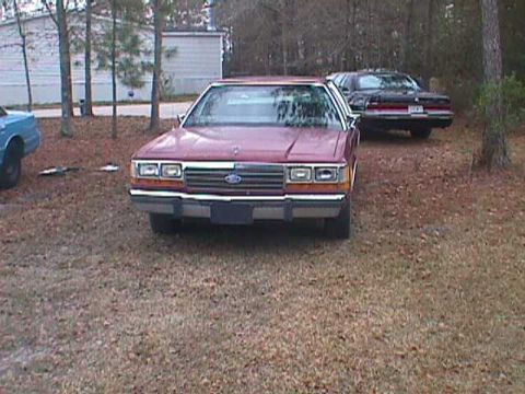 1994 Ford Crown Victoria - A red 1994 Ford Crown Victoria is parked in a yard with another car in the background.