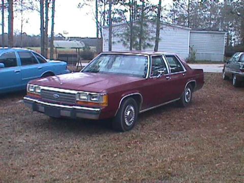 1994 Ford Crown Victoria - Maroon sedan parked on gravel with other vehicles visible in the background.