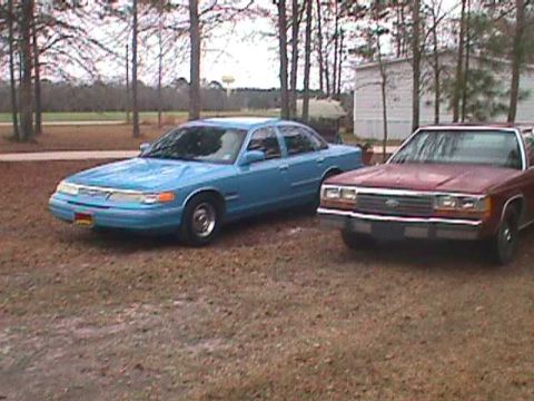 1994 Ford Crown Victoria - Two sedans, a blue 1994 Ford Crown Victoria and a red one, are parked outdoors.