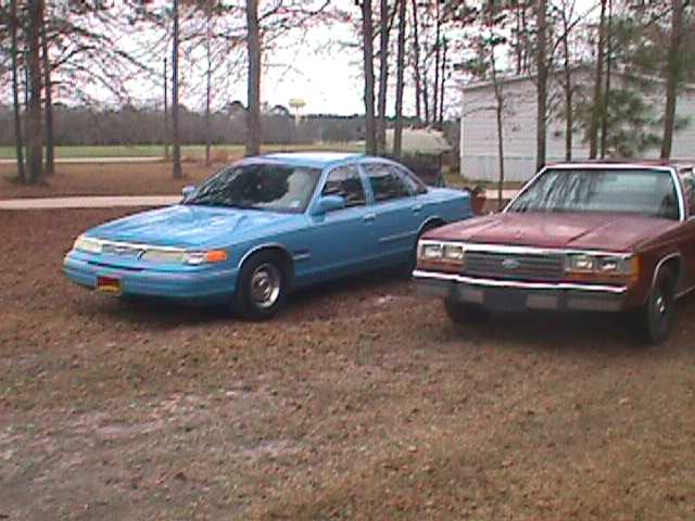 1994 Ford Crown Victoria and a red sedan parked side-by-side on a dirt lot