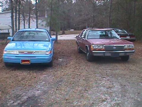 1994 Ford Crown Victoria - A red 1994 Ford Crown Victoria is parked in front of a blue sedan.