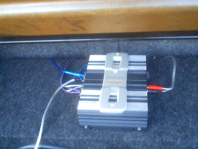 Kenwood car amplifier with wires connected, installed in carpeted trunk