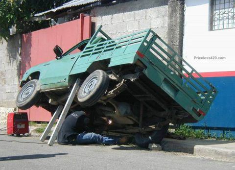 1973 Ford Ranchero - A person is welding the undercarriage of a green pickup truck that is elevated on supports.