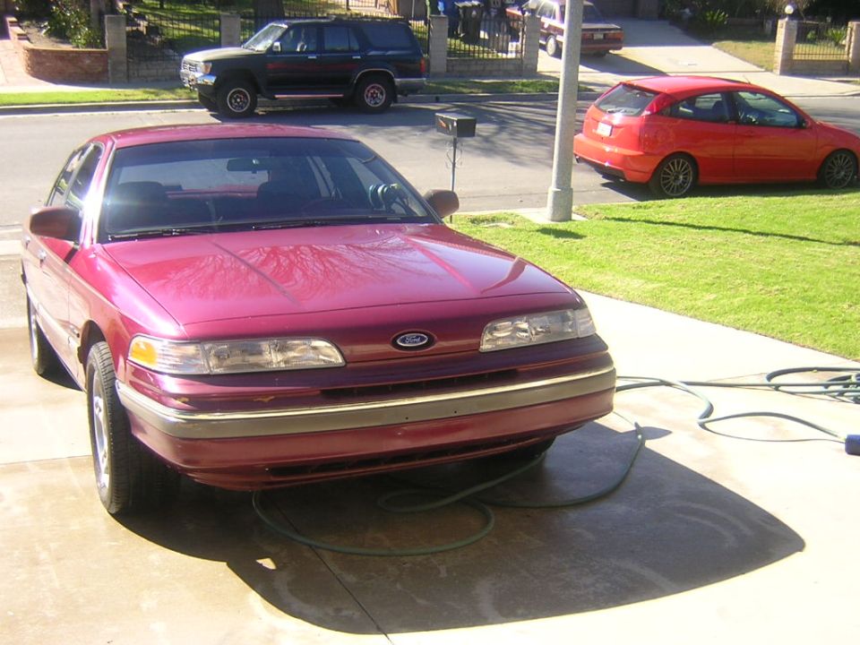 Burgundy Ford sedan parked in driveway, front 3/4 view, with garden hose on the ground.