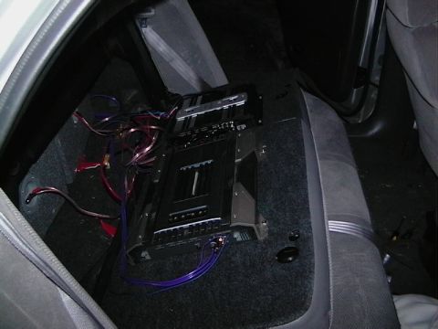 1999 Ford Taurus - An aftermarket audio amplifier is installed in the rear of a car, connected with various wires.