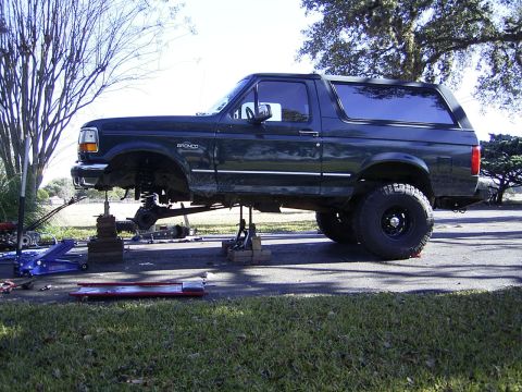1995 Ford Bronco - A dark green 1995 Ford Bronco is elevated on jack stands for maintenance, with its front suspension disassembled.