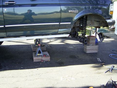 1995 Ford Bronco - A dark green Ford Bronco is shown on jack stands with its suspension disassembled for maintenance.