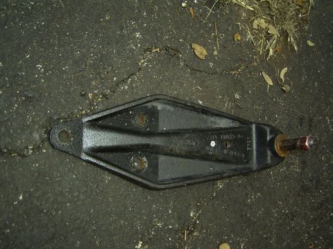 1995 Ford Bronco - A black metal automotive suspension part, possibly from a Ford vehicle, rests on a cracked asphalt surface.