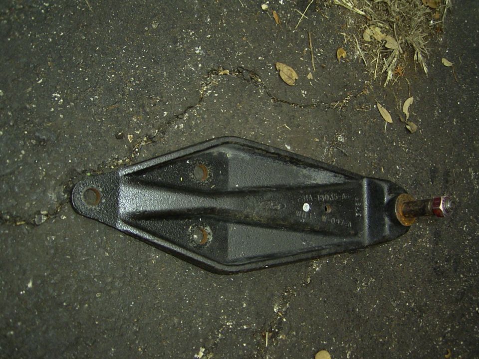 Black cast shock mount bracket with shock stud lying on asphalt