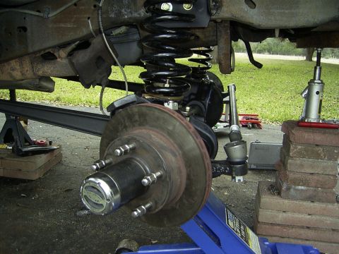 1995 Ford Bronco - Close-up view of the front suspension and wheel hub assembly, showing the coil spring, brake rotor, and steering components.