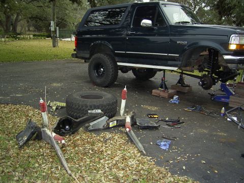 1995 Ford Bronco - A dark green 1995 Ford Bronco is shown with its front suspension disassembled and parts laid out on the ground.