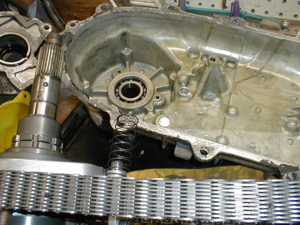 Transfer case disassembled, showing gears, chain, and housing. A spring and bearing are visible inside the casing
