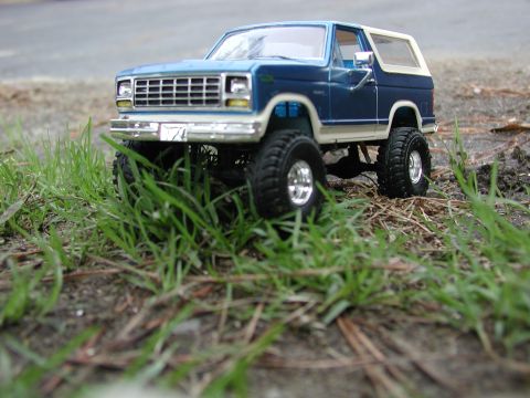 1985 Ford Bronco - A toy model of a blue and white Ford Bronco sits in the grass, its lifted suspension and large tires visible.