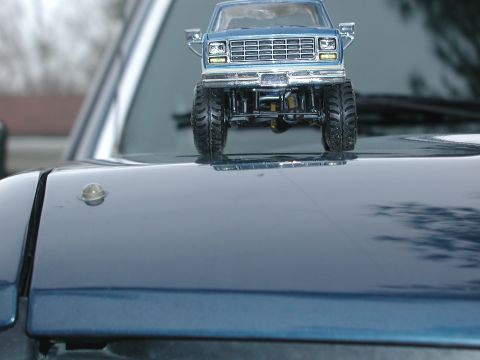1985 Ford Bronco - A toy truck is placed on the hood of a car, with the Supermotors logo visible at the bottom.