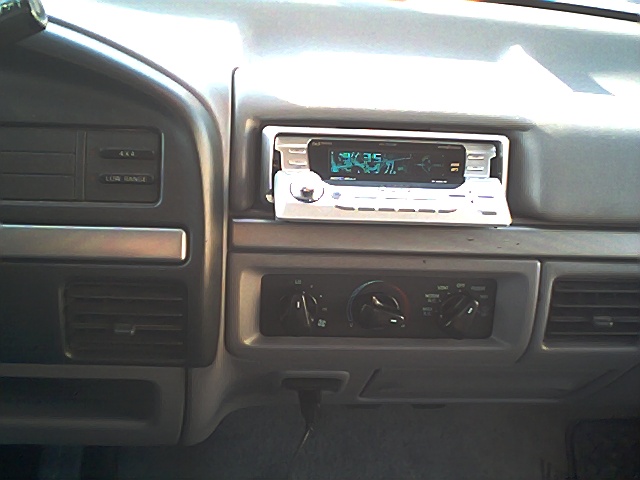Gray dashboard center stack with aftermarket stereo, HVAC dials, and 4x4 indicator lights
