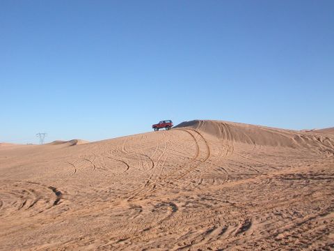 1984 Ford Bronco - 1984 Ford Bronco navigating a sandy dune under a clear blue sky.