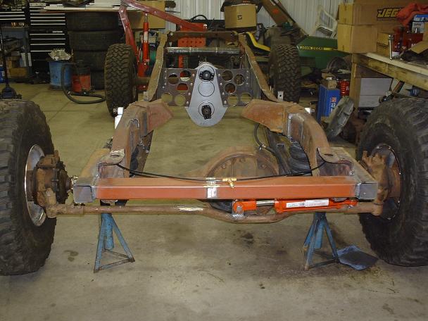 Stripped truck frame on jack stands in garage, rear axle and big tires visible