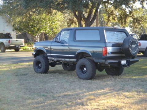 1995 Ford Bronco - A lifted Ford Bronco is parked on a grassy area with a pickup truck in the background.