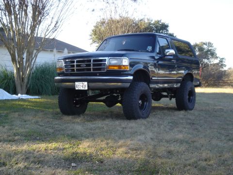 1995 Ford Bronco - A lifted black Ford Bronco sits on a grassy lawn in front of a house and trees.