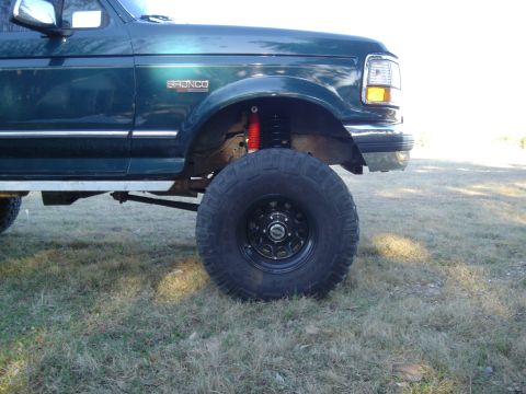 1995 Ford Bronco - This green SUV, identified as a 1995 Ford Bronco, features a lifted suspension and oversized tires for off-road capability.