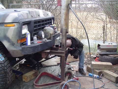 1990 Ford Bronco - A person works on the front end of a camouflaged Ford truck, which appears to be from the late 1970s.