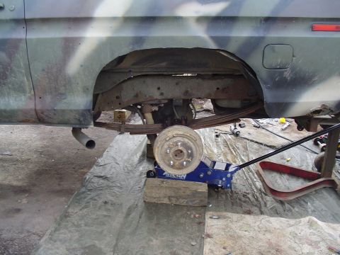 1990 Ford Bronco - Truck is on a jack with the rear wheel off, showing the suspension and axle.