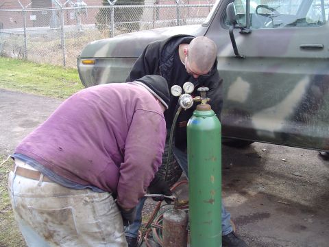 1990 Ford Bronco - Two men are working on a welding apparatus next to a camouflage truck.