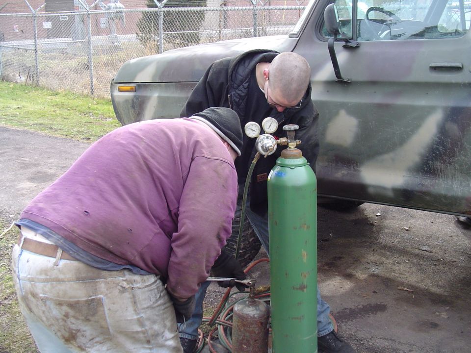 Camouflage truck side view with two men working on welding equipment