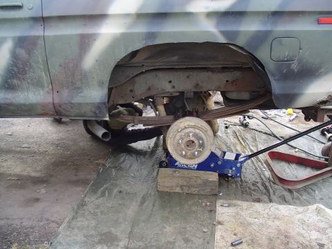 1990 Ford Bronco - A vehicle is being worked on, with the rear wheel removed and supported by a jack.