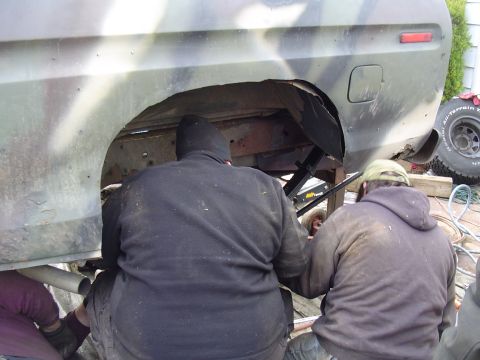 1990 Ford Bronco - People are working on the rear wheel well of a vehicle that appears to be undergoing modifications.